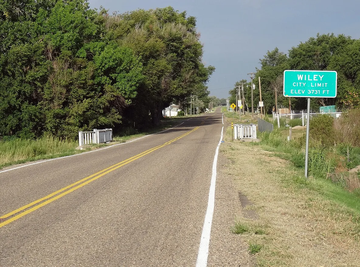 Road entering Wiley, Colorado, with the Wiley city-limit sign beside the roadway.